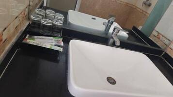 A bathroom with a white sink, a mirror, and a shelf with jars and a pack of tissues.