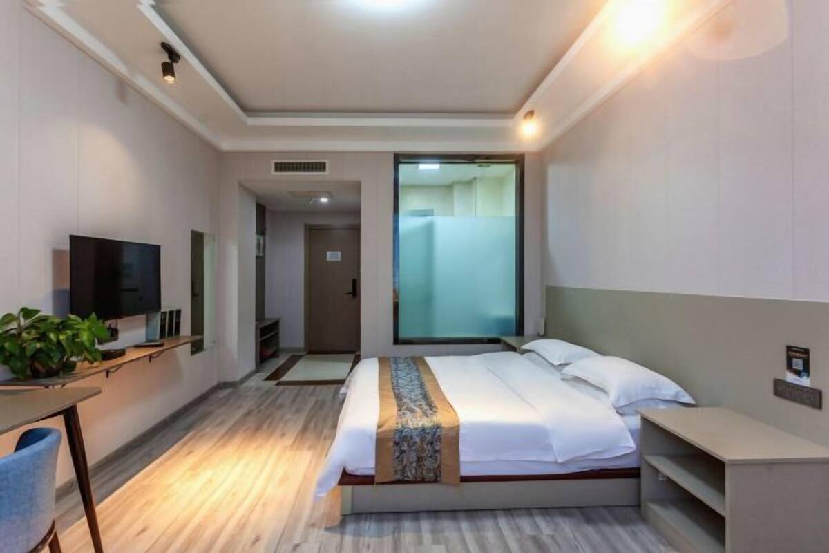 A modern hotel room with a bed, bedside table, TV, and a large window.