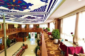 A hotel lobby with a high ceiling, a central atrium, multiple levels, and a dining area with tables and chairs. - Baima Hotel (Damxung)