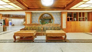 A spacious lobby with a wooden ceiling, a large chandelier, and a central seating area with a sofa and two tables.