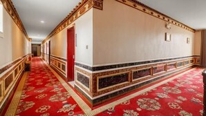 Un pasillo de hotel con alfombra roja, decoraciones elaboradas en la pared y una puerta roja.