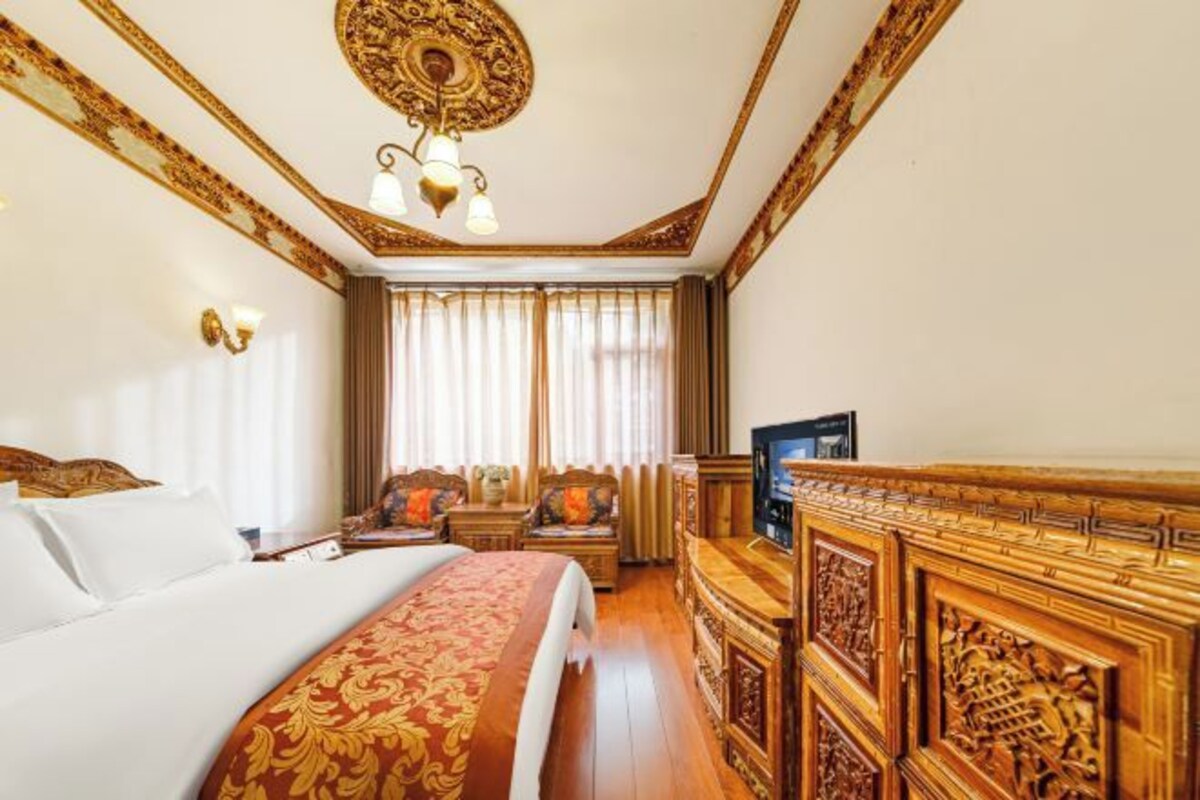 A hotel room with a large bed, a TV, a wooden cabinet, and a decorative ceiling.