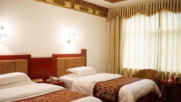 A hotel room with two beds, a wooden headboard, a bedside table with a lamp, and a window with curtains.