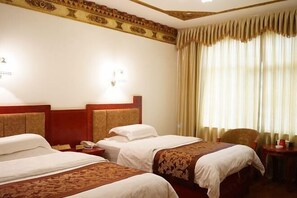 Habitación de hotel con dos camas, cabecero de madera, mesita de noche con lámpara y ventana con cortinas.