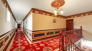 A hallway with a red carpet, a wooden staircase, and a decorative ceiling light fixture.