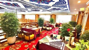 A hotel lobby with a red carpet, wooden furniture, and potted plants.