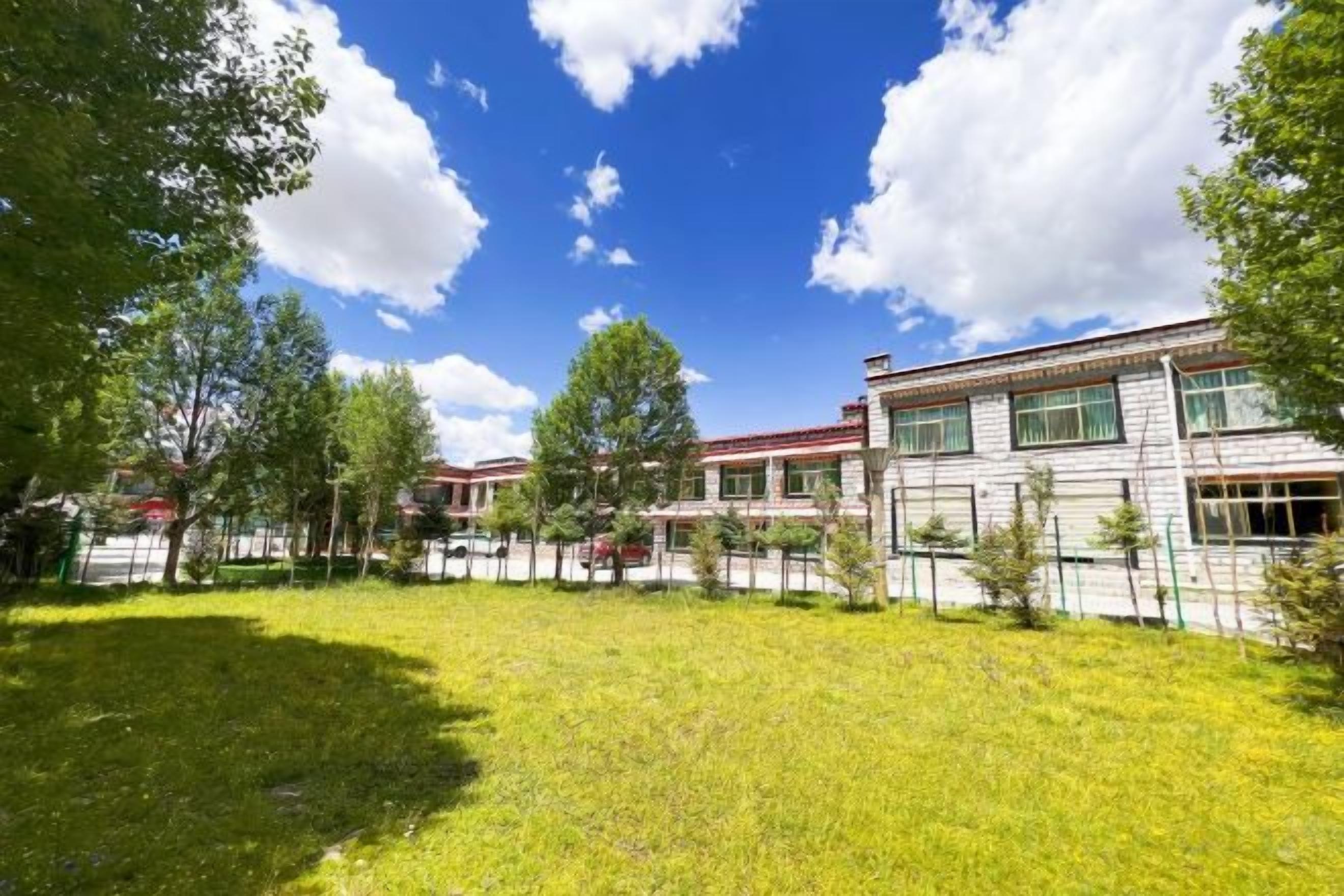 A building with a flat roof, multiple windows, and a fenced courtyard with grass and trees.