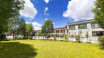 A building with a flat roof, multiple windows, and a fenced courtyard with grass and trees.