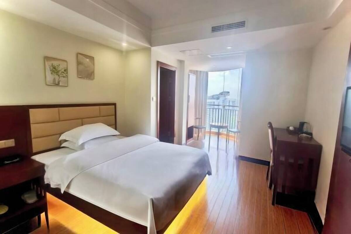 A hotel room with a bed, a desk, and a balcony with a view.