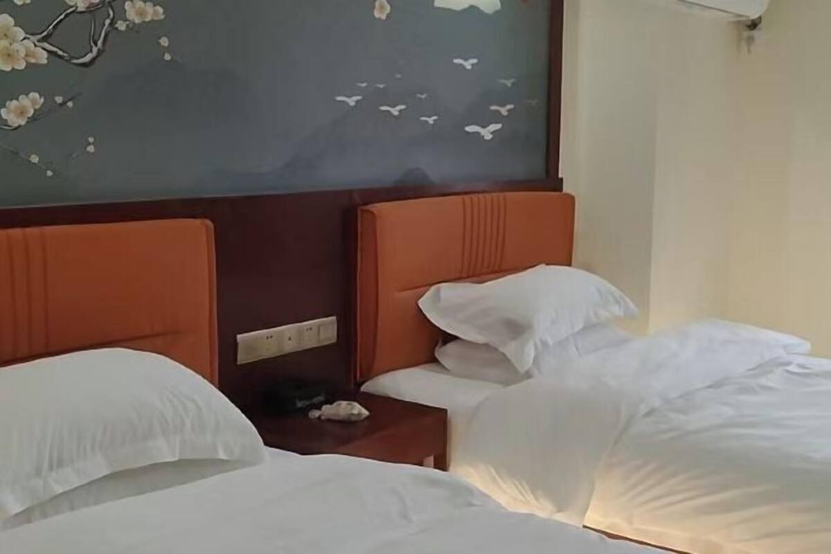 A hotel room with two beds, a nightstand, and a wall with a floral and bird mural.