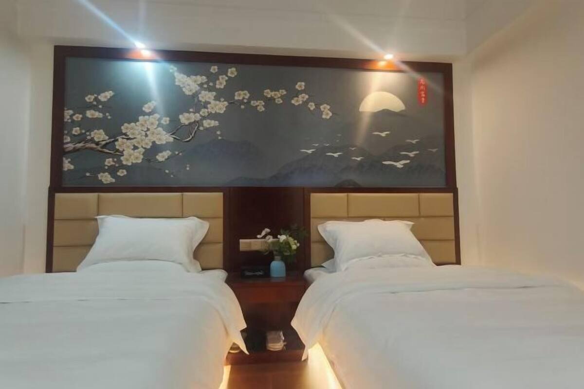 A hotel room with two beds, a large wall-mounted artwork, and a nightstand with a vase.