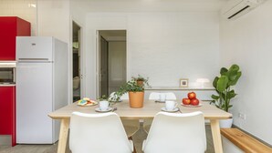 Una cocina moderna con un refrigerador blanco, una mesa de comedor de madera con dos sillas blancas, una planta en maceta y un frutero.