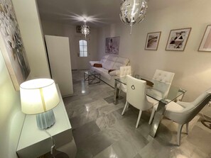 Uma sala de estar moderna com uma mesa de centro de vidro, poltronas de couro branco, um sofá branco e um candelabro.