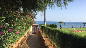 Un sendero conduce a una puerta, bordeado por abundante vegetación y vistas al mar.