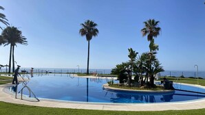 Una piscina con vista despejada al océano, rodeada de palmeras y un césped bien cuidado.
