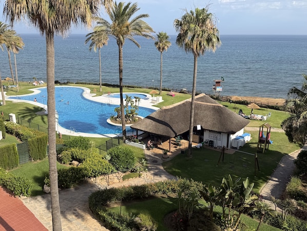 A resort with a swimming pool, palm trees, and a view of the ocean.