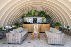 A covered outdoor seating area with wicker furniture, a central round table, and a bar with a stone backdrop.