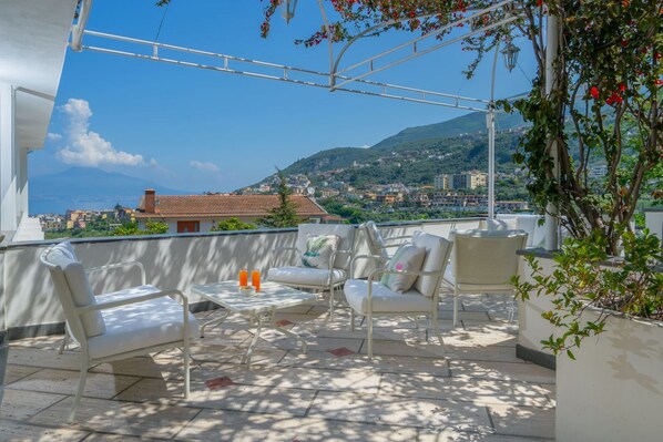 A rooftop terrace with outdoor seating and a view of a coastal town.