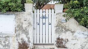 A white gate with blue decorative elements, leading to a concrete entrance with steps.