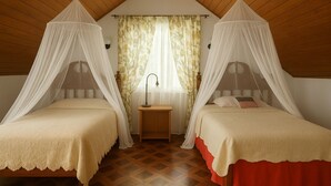 Ein Schlafzimmer mit zwei Betten, jeweils mit Baldachin, Nachttisch und einem Fenster mit floralem Vorhang.