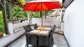 A patio with a table and chairs, an umbrella, and a bottle of water. - Neles Kate am Diemelsee by Interhome (Marsberg)