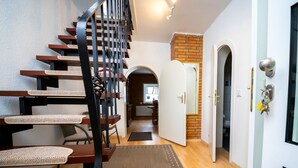 A staircase with a black metal railing, a wooden floor, and a rug leading to a room with a white door and a brick wall. - Neles Kate am Diemelsee by Interhome (Marsberg)