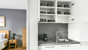 Una kitchenette compacta con un lavamanos integrado, cafetera y estante con ollas y tazas.