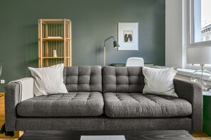Una sala de estar moderna con un sofá gris, una estantería de madera, una obra de arte enmarcada y un escritorio con una lámpara.