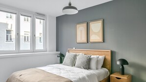 Un dormitorio con una cama, dos mesitas de noche, una ventana y dos cuadros colgados en la pared.