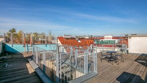 Ein Poolbereich auf dem Dach mit Holzterrasse, Metallgeländern und Blick auf die Stadtlandschaft.