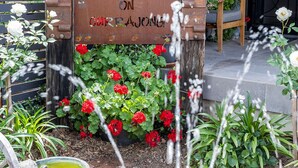 A garden with a fountain, a wooden sign, and a bench. - Cabos On Currajong! (Parkes)