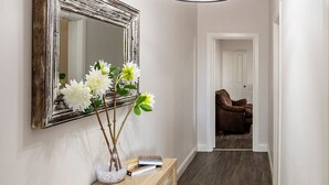 A hallway with a wooden console table, a mirror, and a hanging light fixture. - Cabos On Currajong! (Parkes)