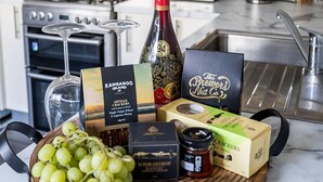 A kitchen counter with a wooden board holding grapes, a bottle of wine, and various food items. - Cabos On Currajong! (Parkes)