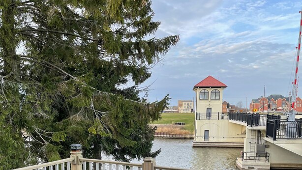 Una terraza con mobiliario de mimbre con vista a una masa de agua, un edificio pequeño con techo rojo y una barandilla blanca.