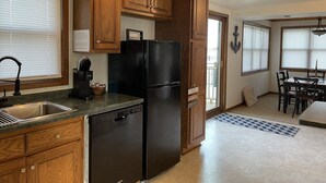 Una cocina con armarios de madera, un refrigerador negro, un lavavajillas y una zona de comedor con una mesa y sillas.