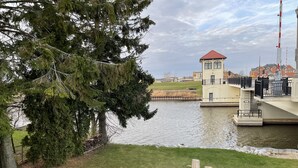 Vista al lago con una terraza de madera, un hogar para fogata y un pequeño edificio con techo rojo.