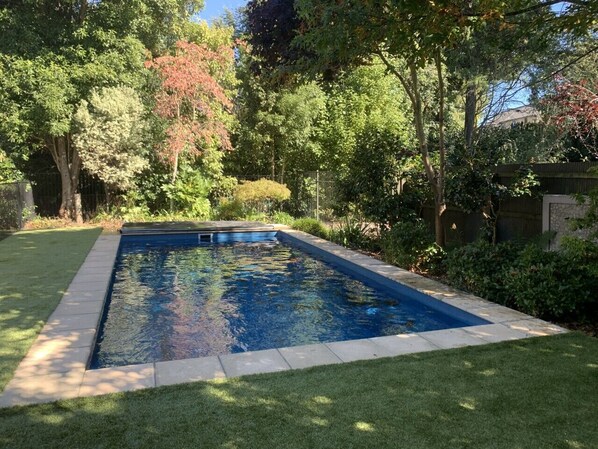 A rectangular swimming pool with a tiled edge, surrounded by a well-maintained lawn and various trees.