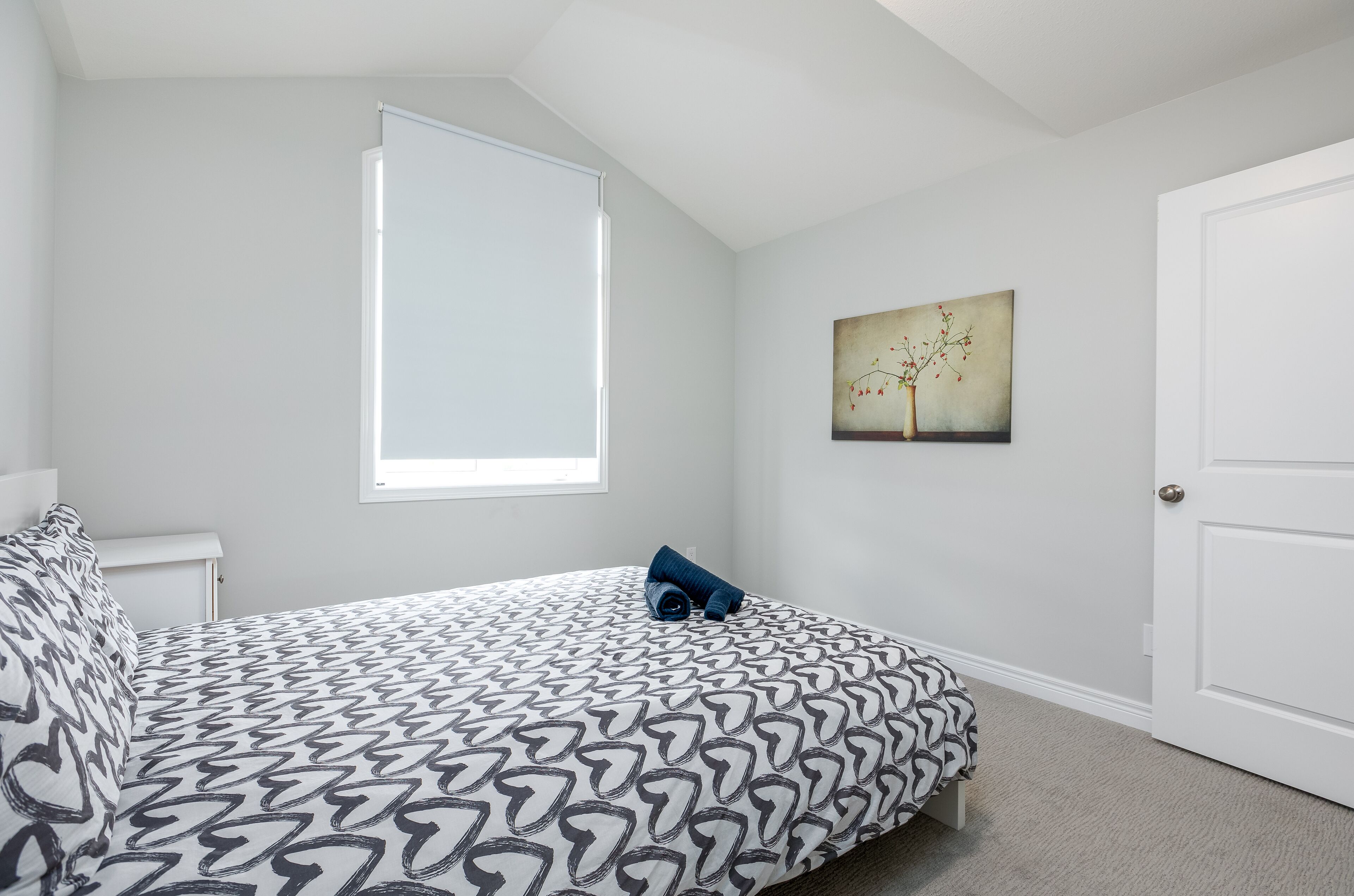 A bedroom with a bed, a window, a door, and a painting on the wall.