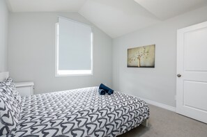 A bedroom with a bed, a window, a door, and a painting on the wall.