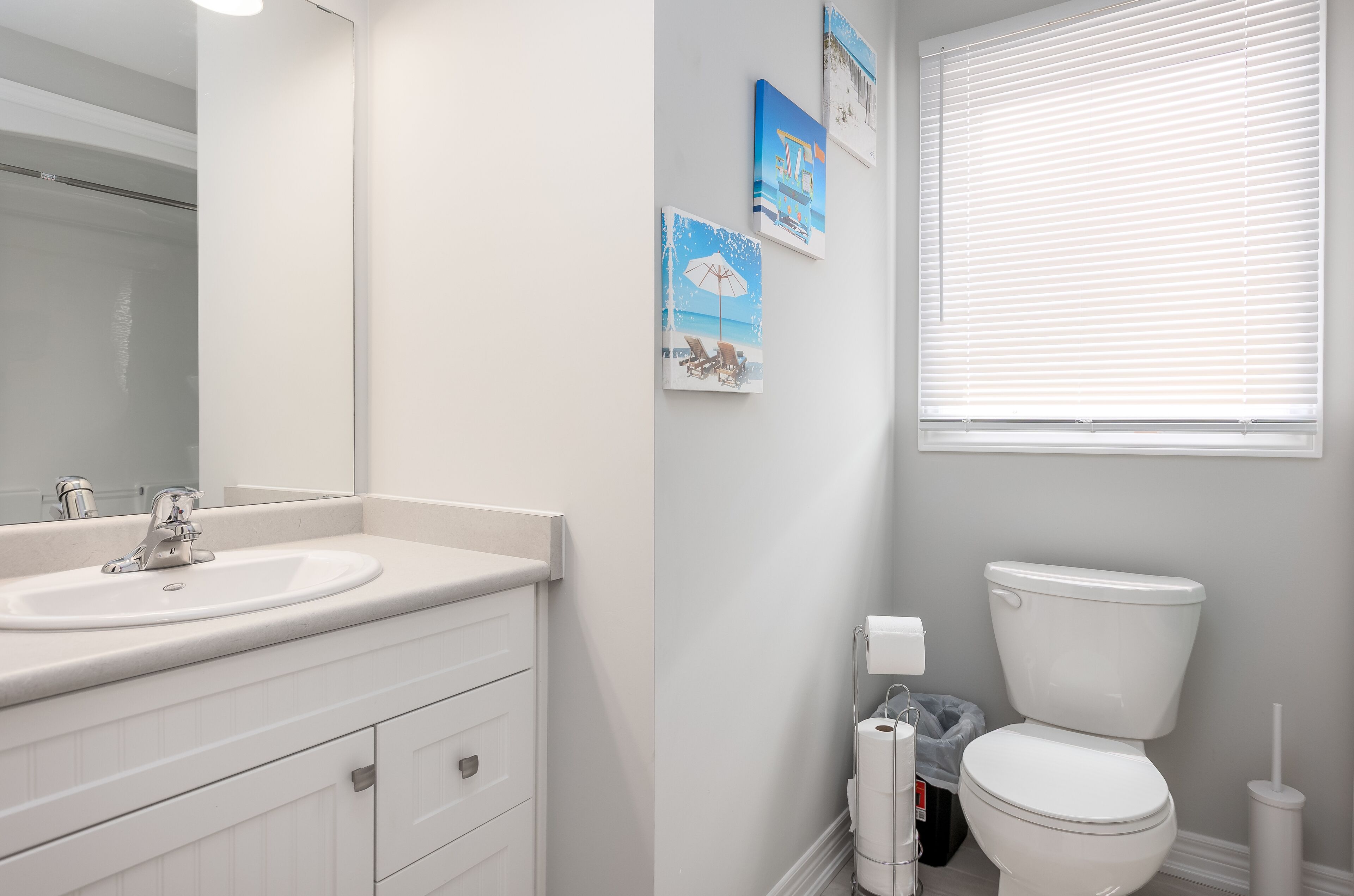 A bathroom with a white sink, mirror, and toilet. There are three framed pictures on the wall.