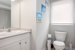 A bathroom with a white sink, mirror, and toilet. There are three framed pictures on the wall.