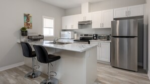 A modern kitchen with white cabinets, stainless steel appliances, a marble countertop, and two black bar stools. - Luxury Entire house mins Niagara falls & Brock uni (Thorold)