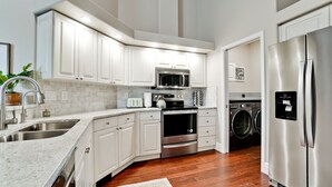Una cocina moderna con armarios blancos, electrodomésticos de acero inoxidable, horno empotrado, microondas y refrigerador.