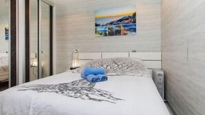 Un dormitorio moderno con una cama grande, un cuadro de una escena costera y un ventanal corredero.