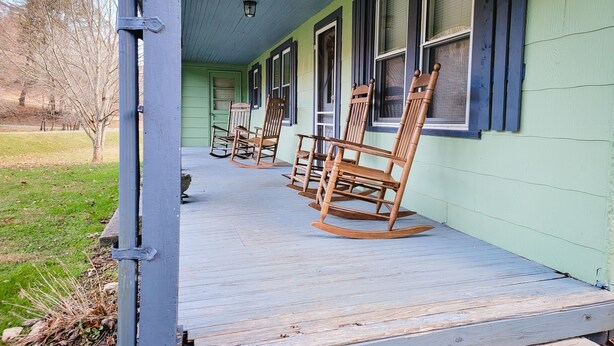 A porch with wooden rocking chairs and a green exterior wall. - New River Cottage (Crumpler)