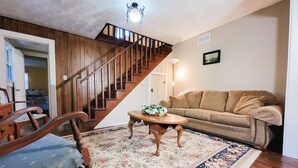 A living room with a wooden staircase, a sofa, a coffee table, and a patterned rug. - New River Cottage (Crumpler)