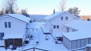 Een besneeuwd woongebied met twee huizen, een houten terras en uitzicht op een meer.