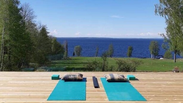 A wooden deck with two green yoga mats and pillows, overlooking a body of water.