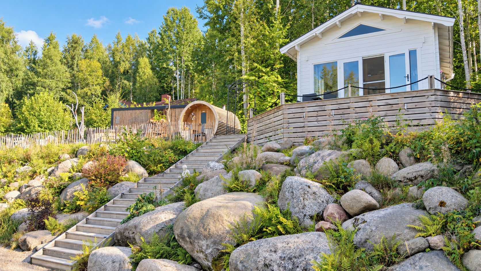 Una cabaña con una escalera de madera que lleva a una terraza, rodeada de grandes rocas y follaje.