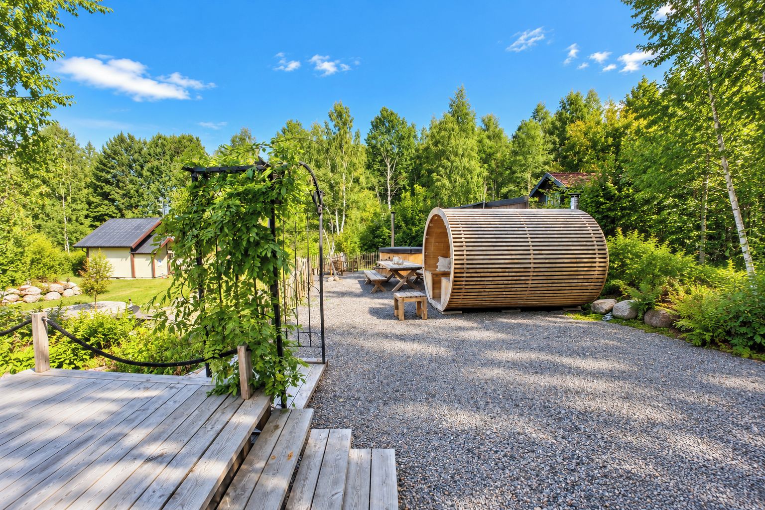 A wooden deck leading to a relaxation area with a large cylindrical structure, surrounded by trees and a small building.